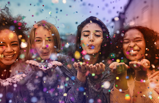 multicultural women blowing glitter and sparkles into the camera