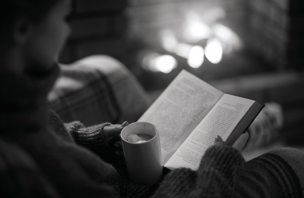 Sense of hygge with woman cozy next to fireplace with book and coco