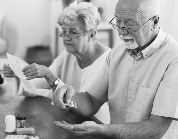 Frau liest Packungsbeilage zu Medikamenten die älterer Mann einnimmt