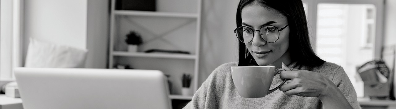 A woman holding a mug looks at a laptop