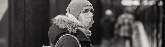 A person with a mask, hat and furred hood looks back at the camera.
