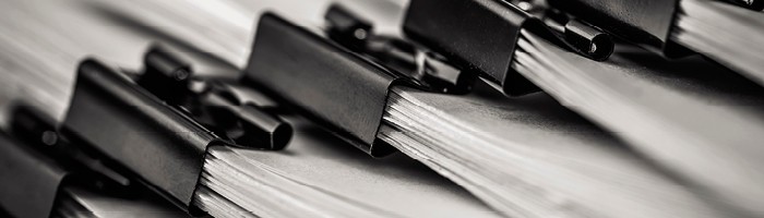 A closeup of several stacks of paper in black binder clips.