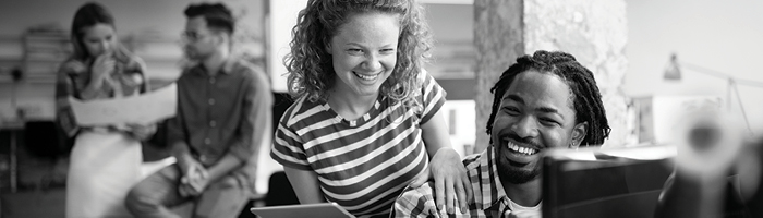 Two people laughing in front of a desktop computer