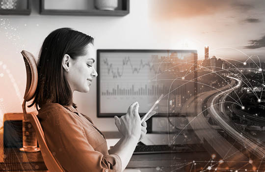 A person sits at a workstation using technology next to an image of a city, depicting the relationship between technology and modern society. 