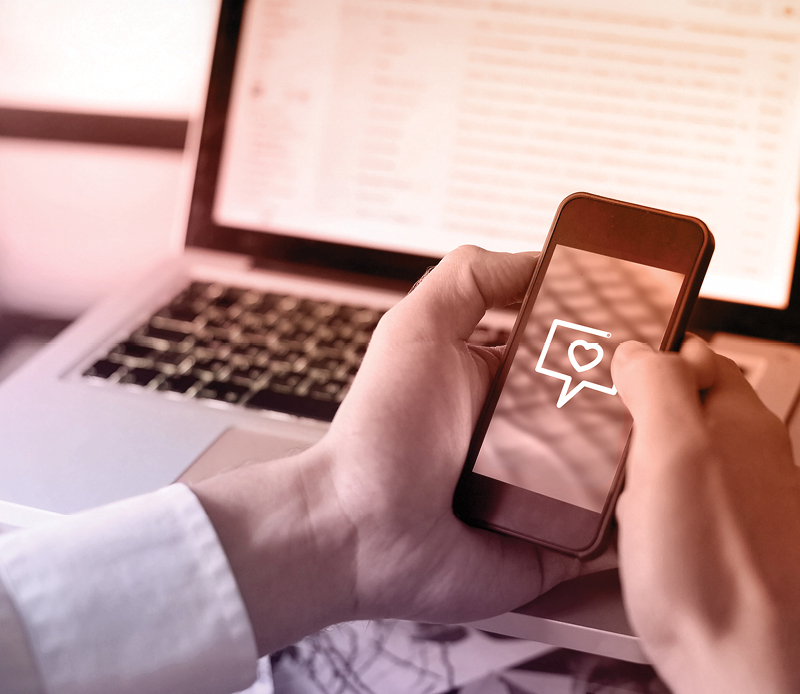 A user tapping on a phone before a laptop computer