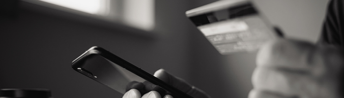 A hand holding a mobile phone. The other hand is holding a credit card.