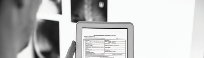 A medical professional examines a tablet of data with x-rays visible in the background.