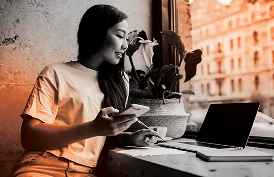 Woman writing with a pencil while working with 2 screens