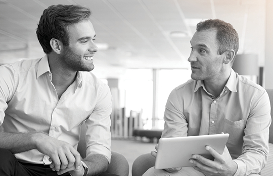 A man talking to a colleague with a tablet on hand